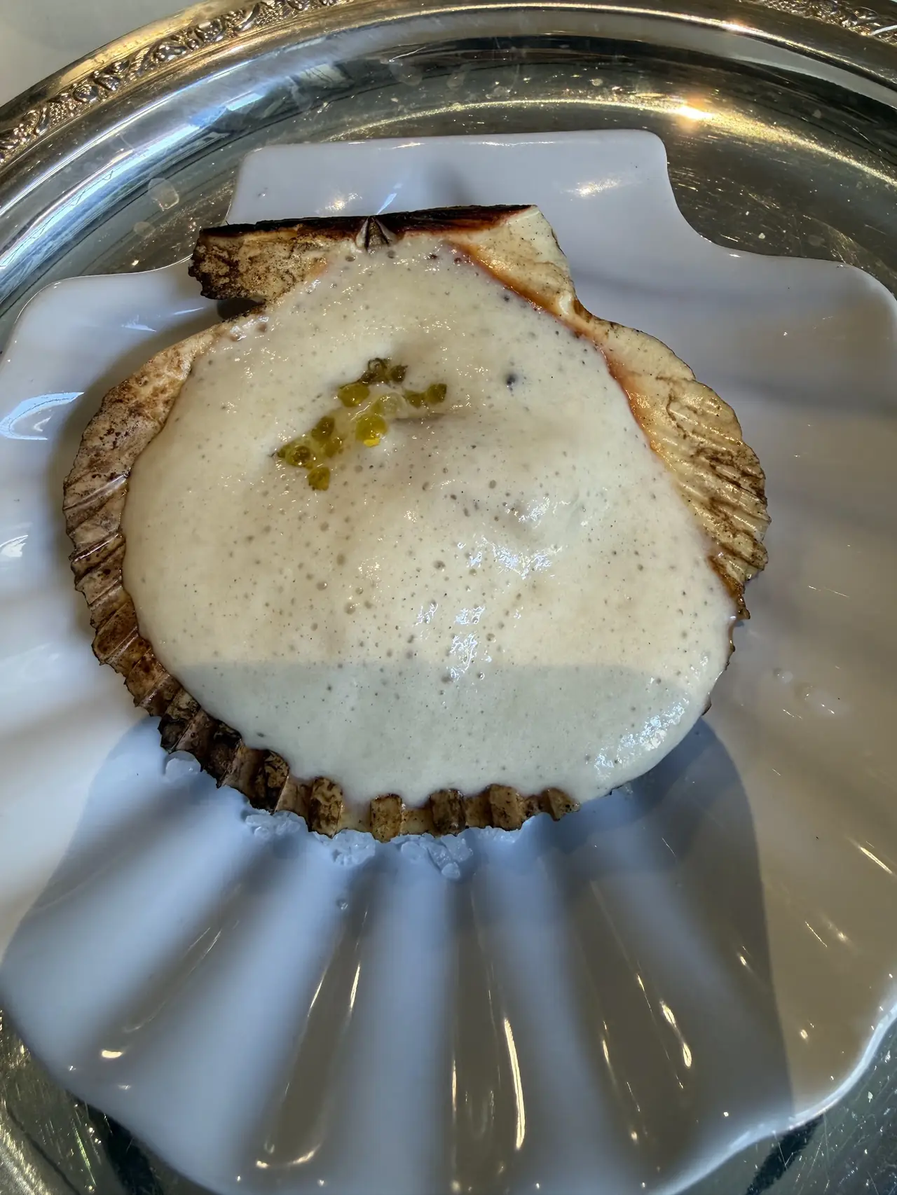 Scallop served in its shell with a creamy foam sauce and green roe garnish