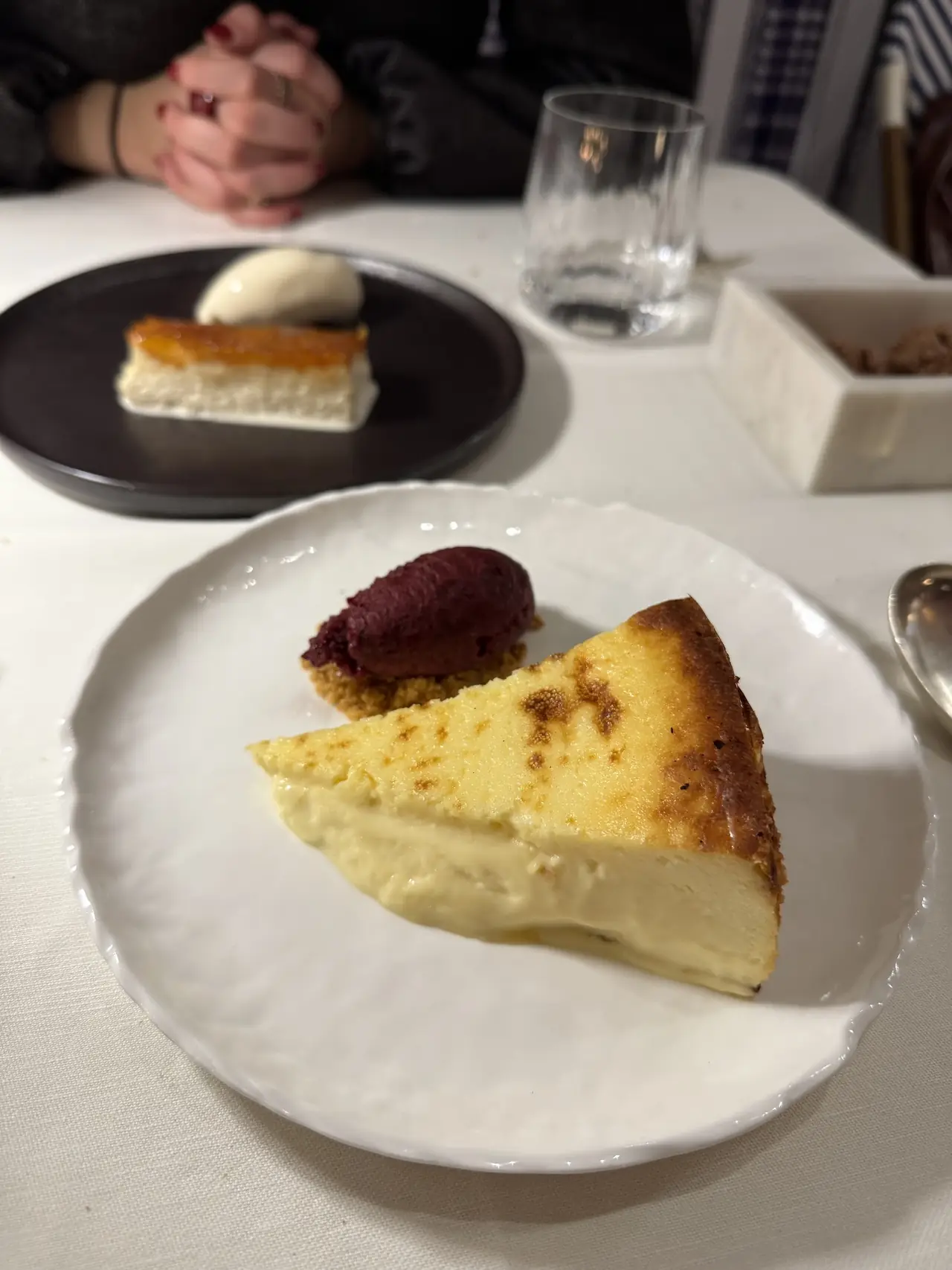 Wedge of baked cheesecake with a scoop of berry sorbet, a second dessert plate visible in the background