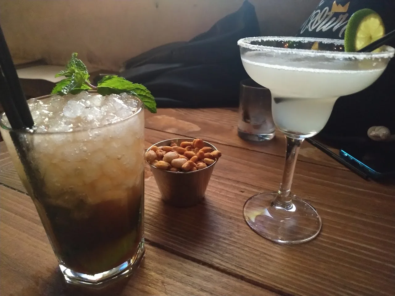 A margarita and a dark cocktail on a wooden table with peanuts