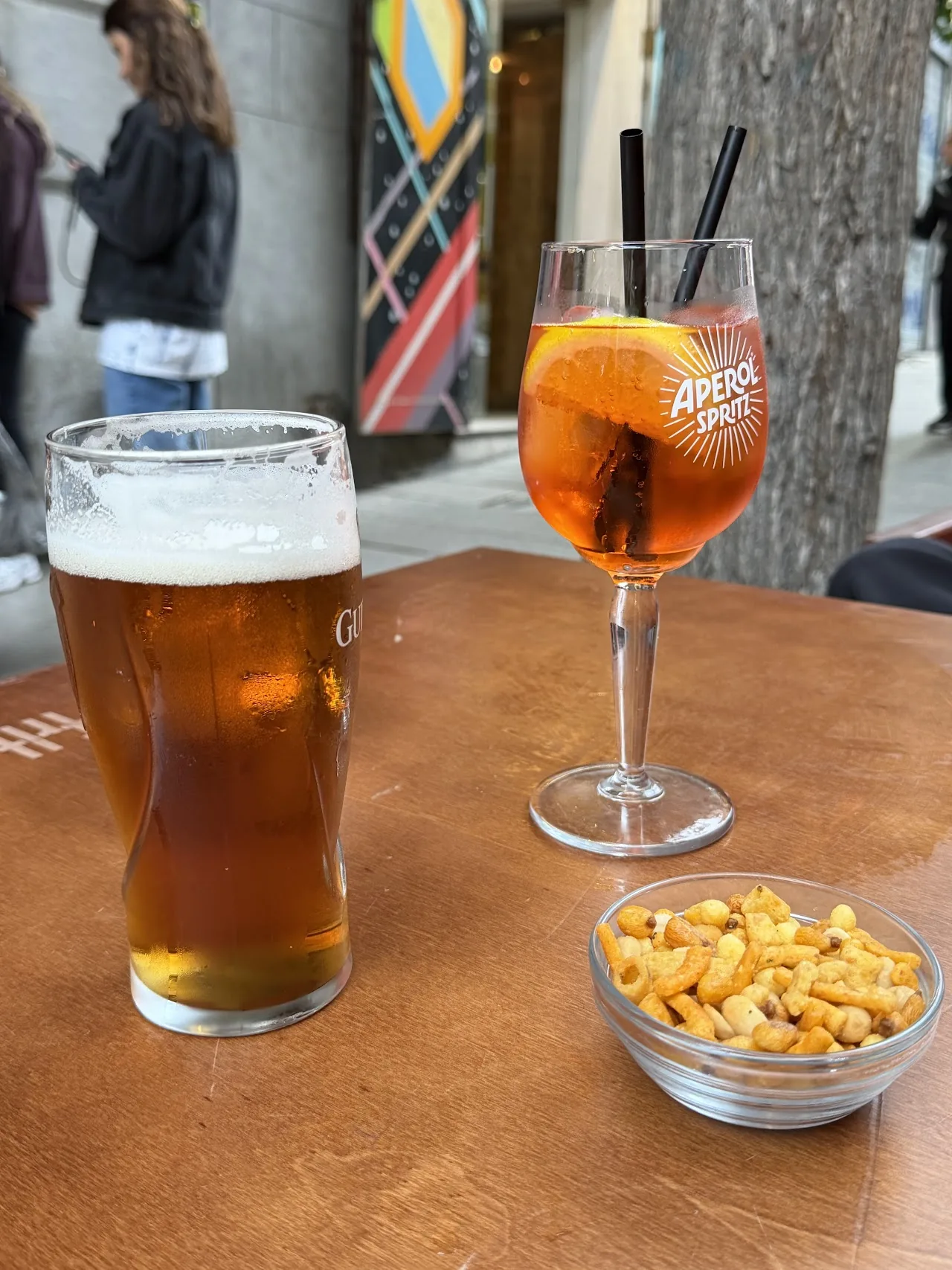 A glass of beer next to an orange spritz cocktail with nuts