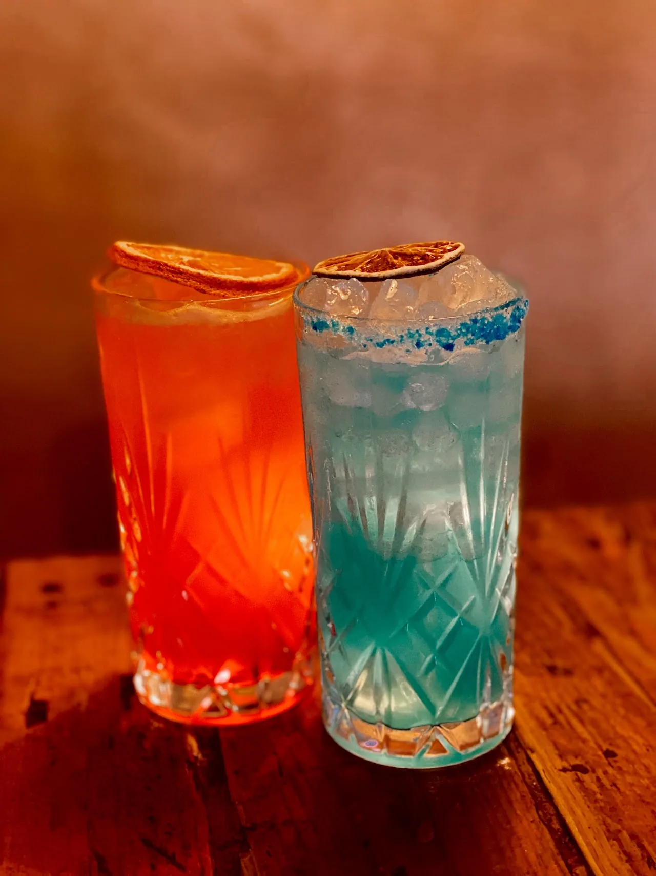 Two colorful cocktails, one orange and one blue, on a table