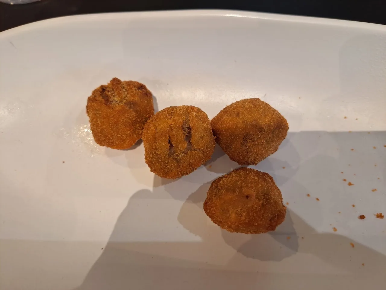 Four golden fried croquettes on a white plate