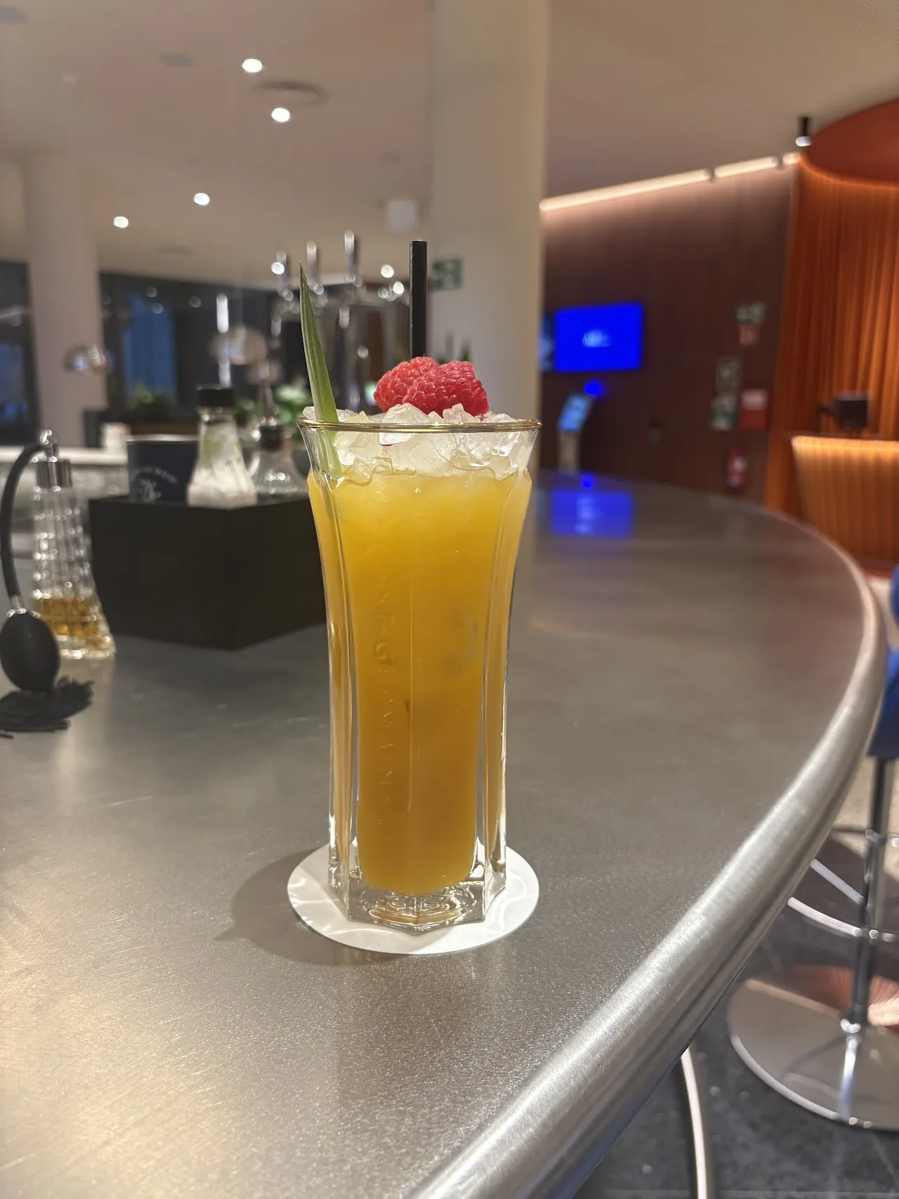 A tall glass of an orange cocktail with a straw on a bar counter