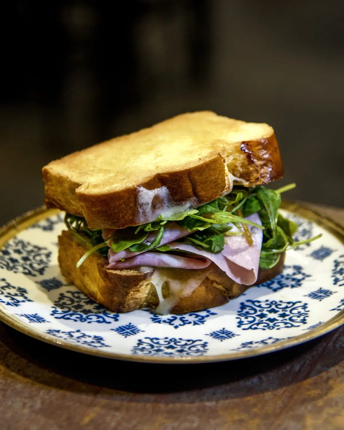 Toasted sandwich with ham, melted cheese and arugula on patterned plate