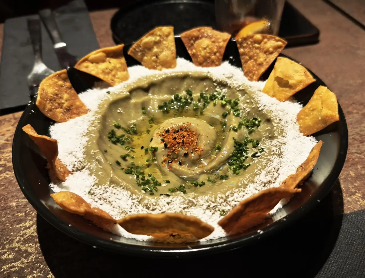 Bowl of green dip with chives and spice, ringed with fried wonton chips