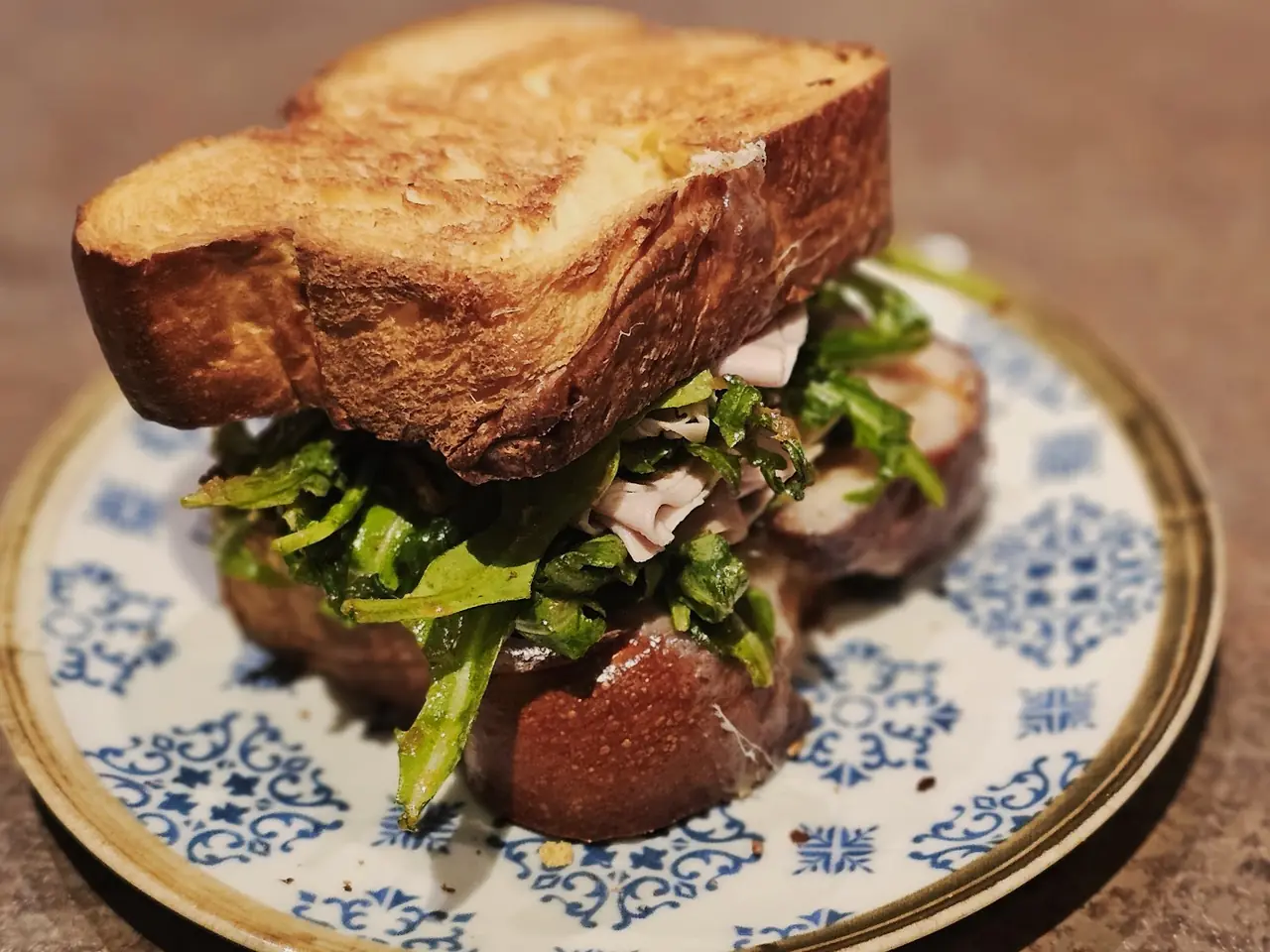 Toasted sandwich with sliced meat and arugula on patterned plate