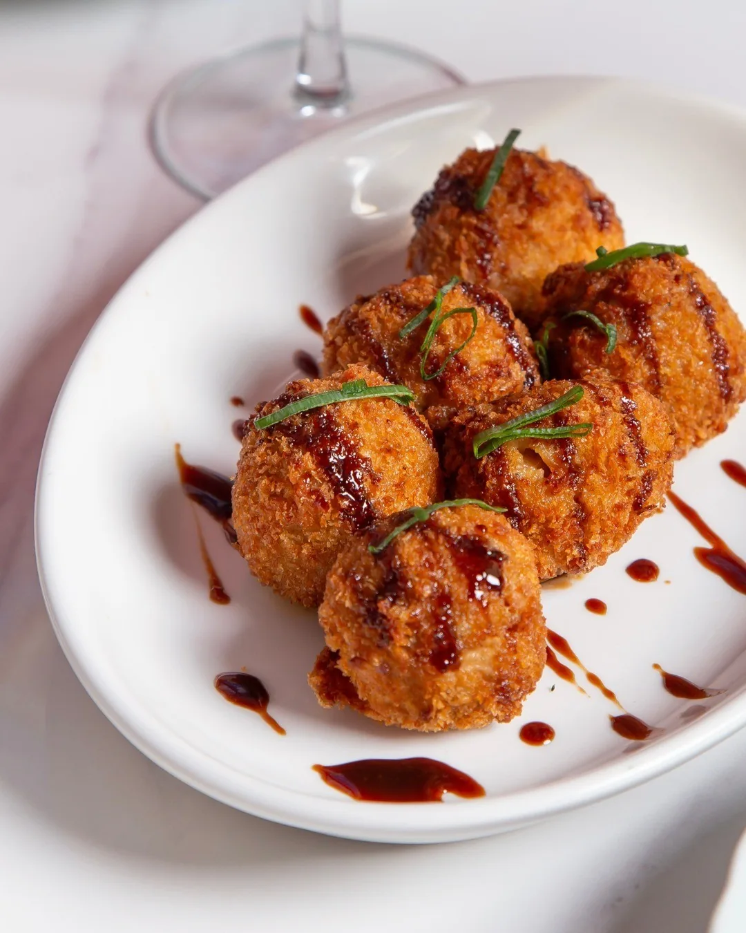 Four glazed fried balls with a dark sauce on a white plate