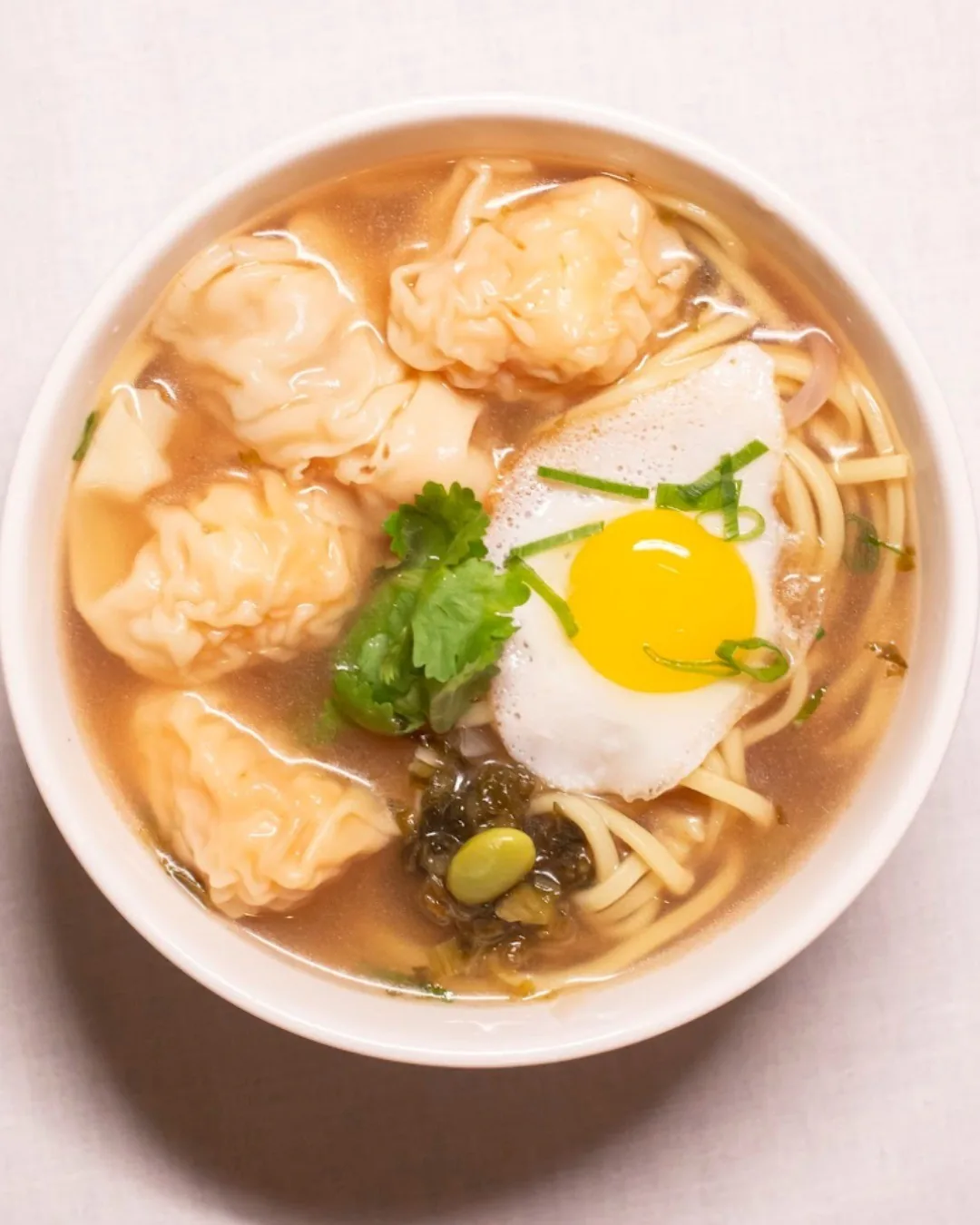 A bowl of noodle soup with dumplings and a fried egg