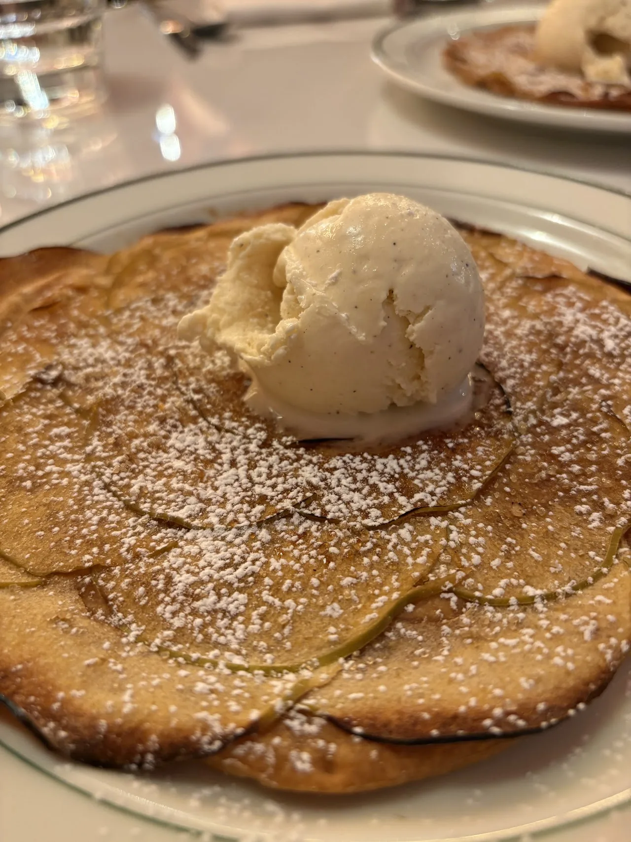 A folded pancake dessert topped with a scoop of ice cream and powdered sugar