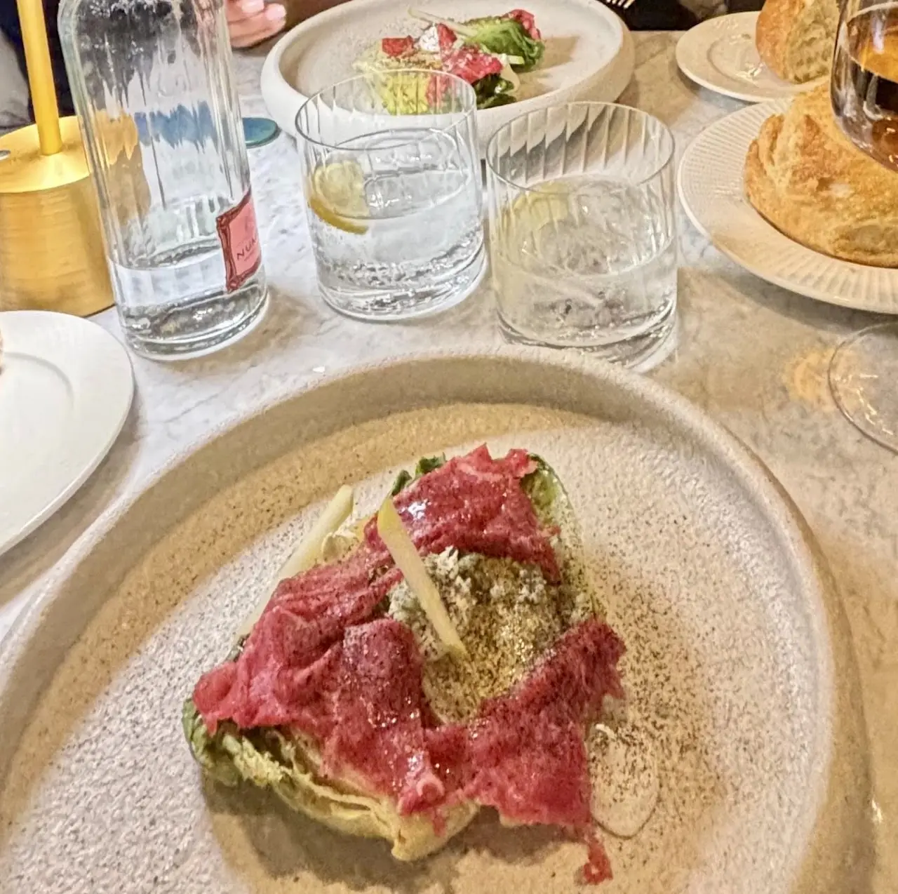 Thin slices of raw beef with a herb sauce and shaved cheese on a plate.