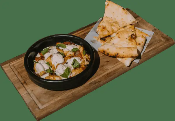 Baked mushrooms in a bubbling cheese sauce with fresh mint, served with charred grilled flatbread on a wooden board at Grosso Napoletano Senza Glutine