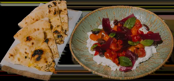 Charred flatbread triangles beside a plate of burrata topped with cherry tomatoes, roasted red peppers, olives, and mint at Grosso Napoletano Senza Glutine