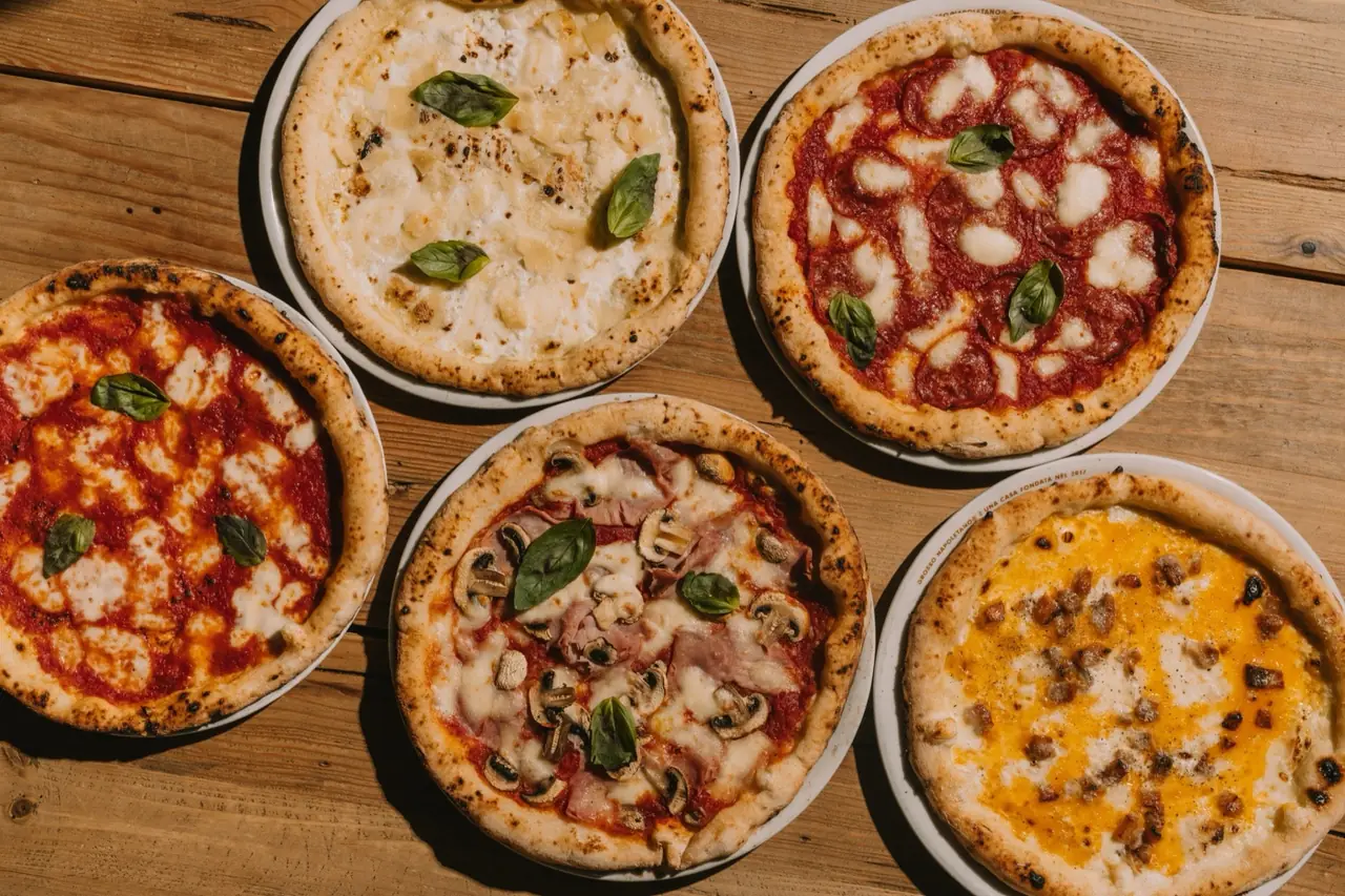 Five round Neapolitan-style pizzas with varied toppings — cheese and pear, pepperoni, margherita, mushroom and ham, and a yellow cheese blend — arranged on a wooden table at Grosso Napoletano Senza Glutine