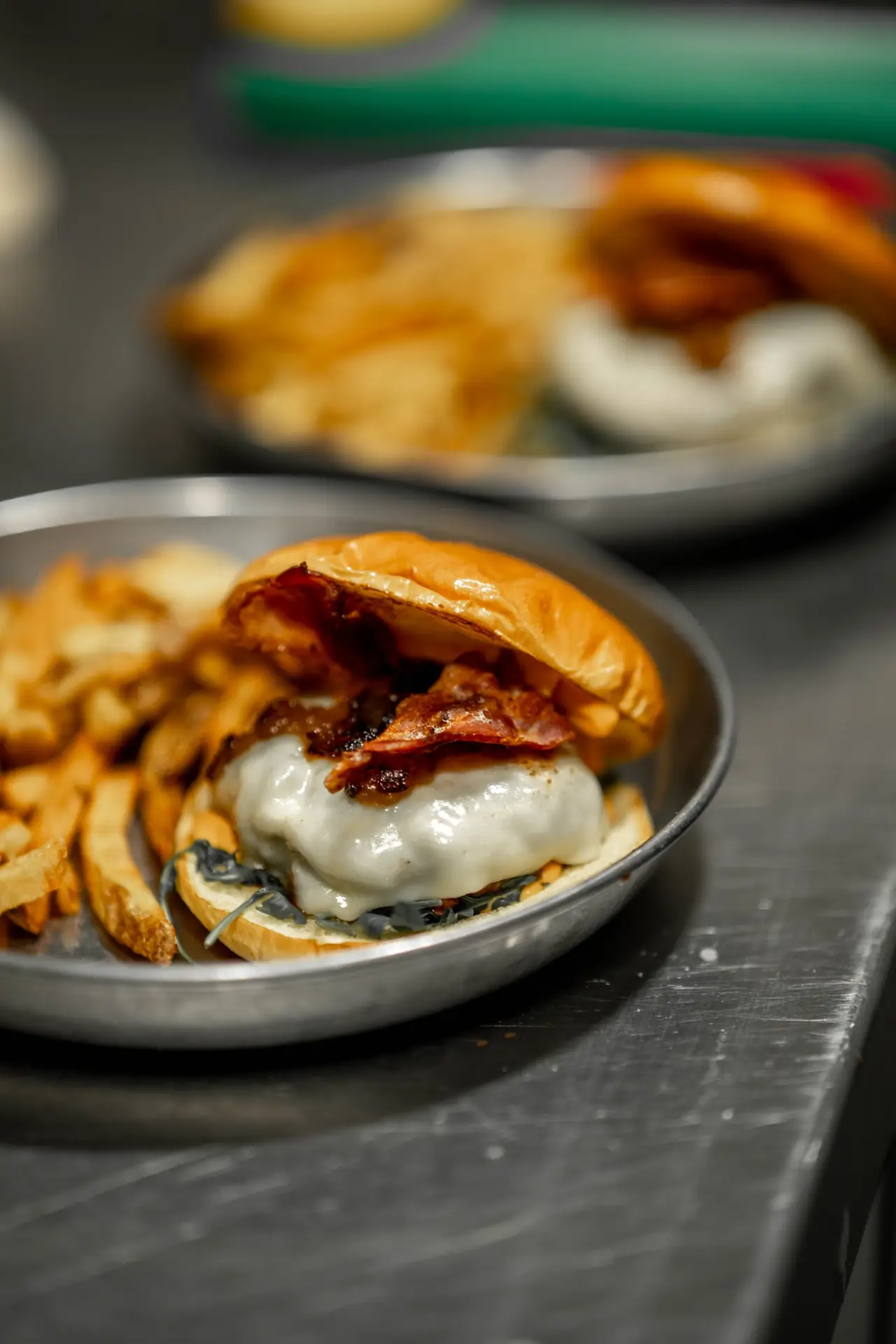 Bacon cheeseburger with melted cheese and a side of fries on a metal plate