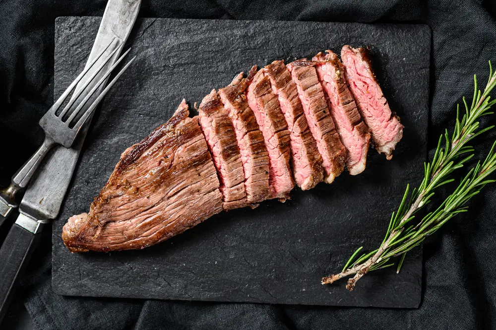 Sliced grilled steak fanned out on a slate board with a rosemary sprig.