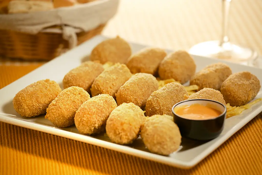 A plate of breaded croquettes with a small bowl of dipping sauce.