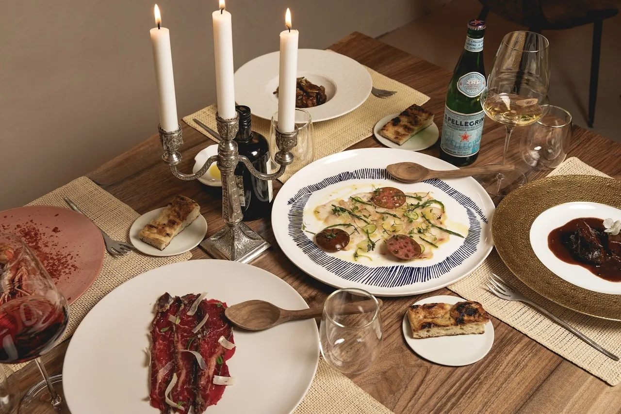 A candlelit table set with several plated dishes, wine glasses and a carpaccio