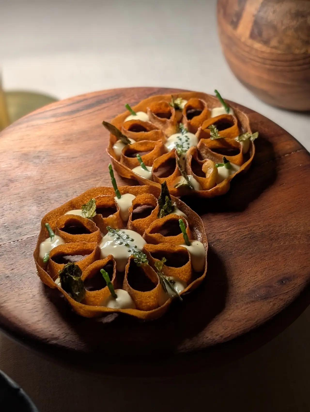 Two woven pastry basket dishes filled with sauce, caviar and herb garnish on a wooden board