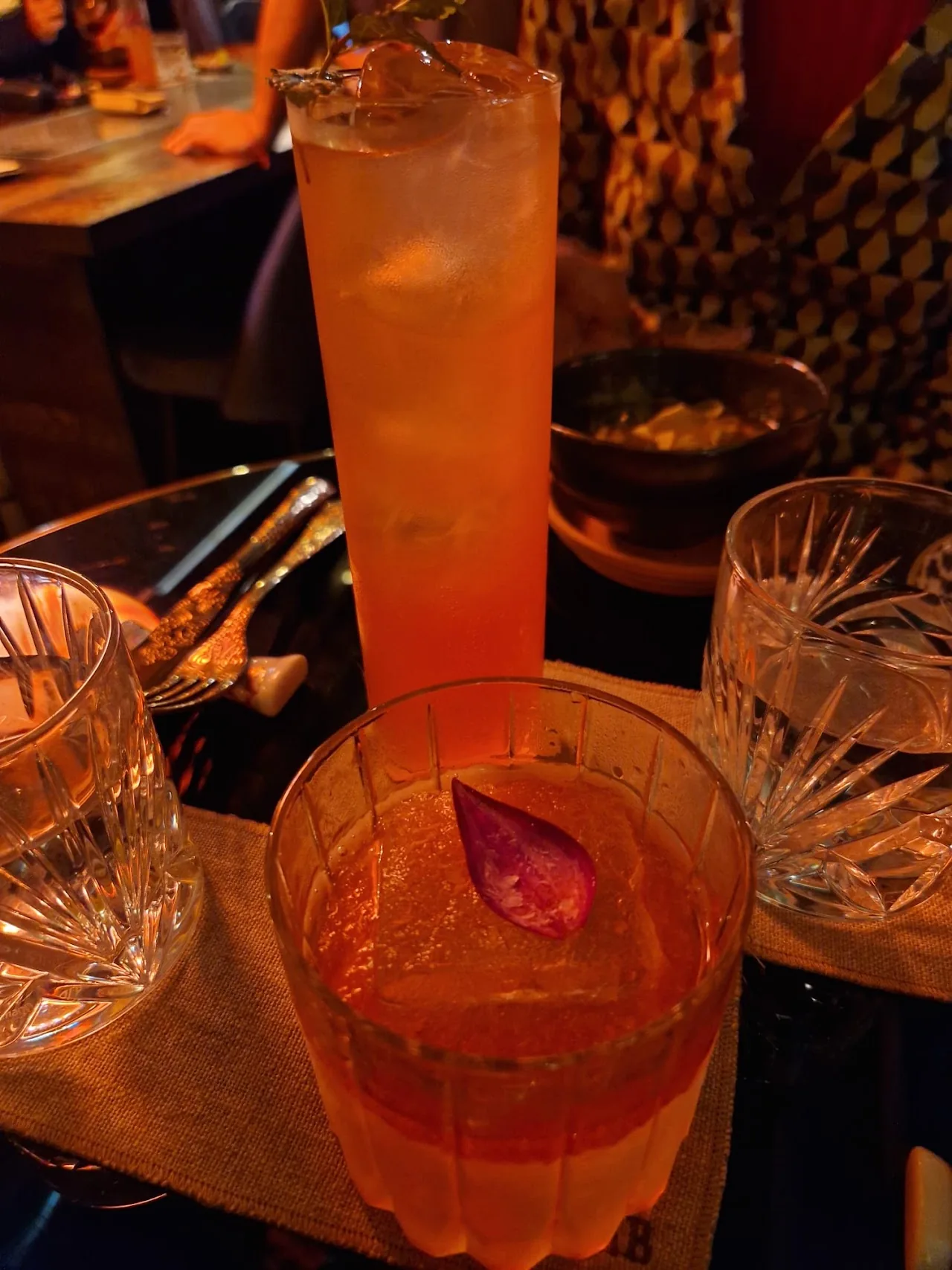 A tall orange cocktail with ice in a glass tumbler