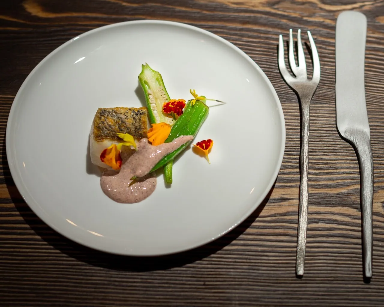 A plated fish dish with edible flowers and a pink sauce swirl