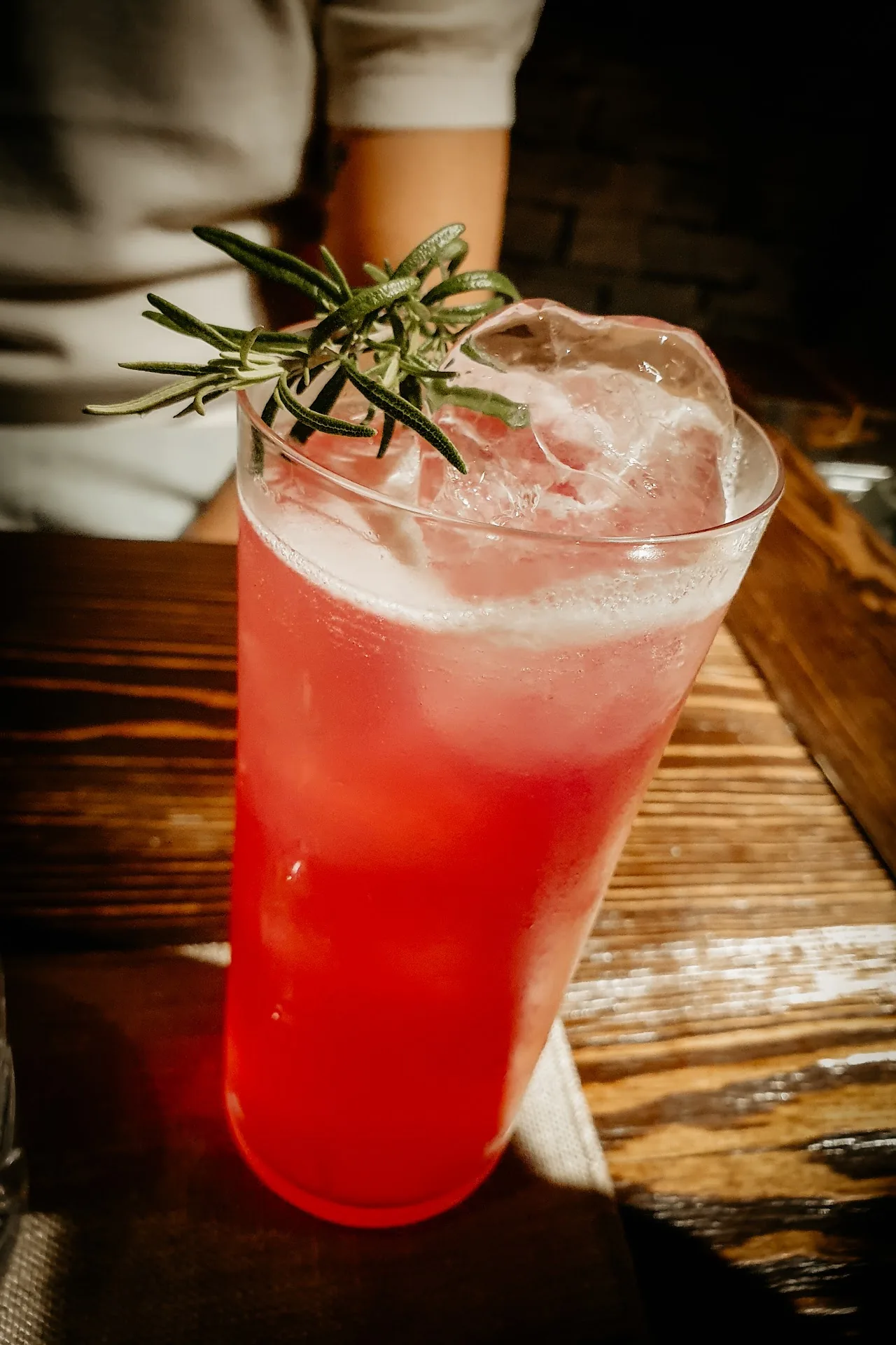 A red cocktail garnished with a rosemary sprig