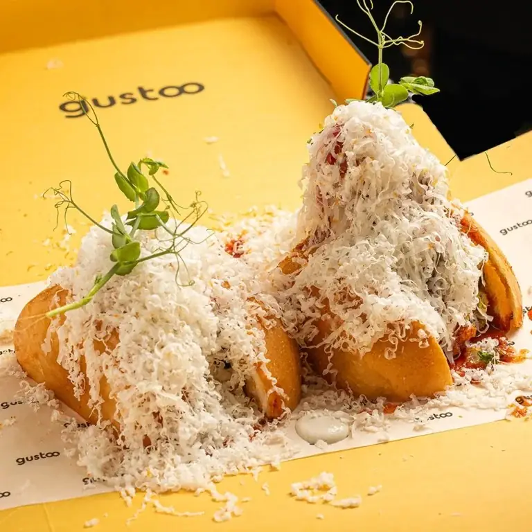 Fried bread pockets buried under a mound of finely grated cheese with pea-shoot garnish, on branded yellow packaging