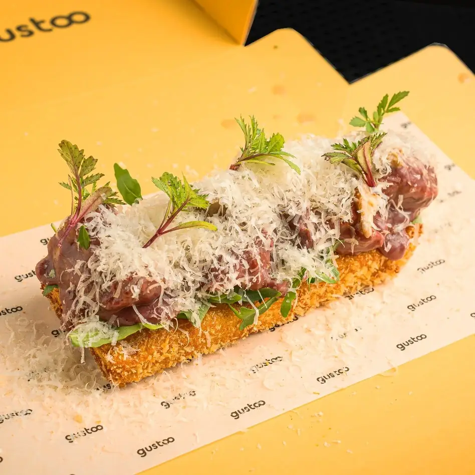 Crumbed fried bar topped with cured meat, grated cheese and fresh herbs on branded paper