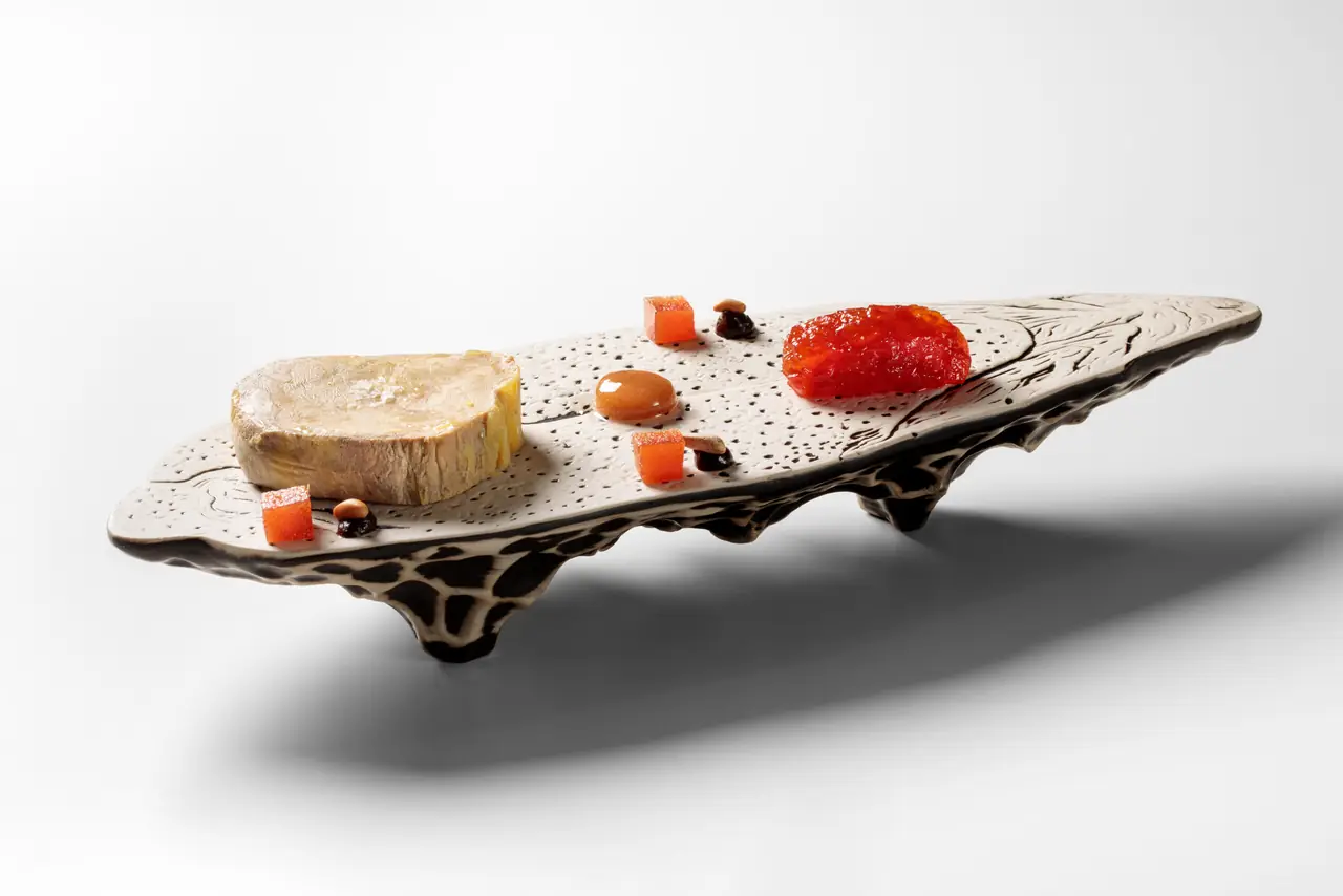 Foie gras terrine with tomato jam, apricot jelly cubes, and a caramel drop on a hand-carved ceramic plate at Gut