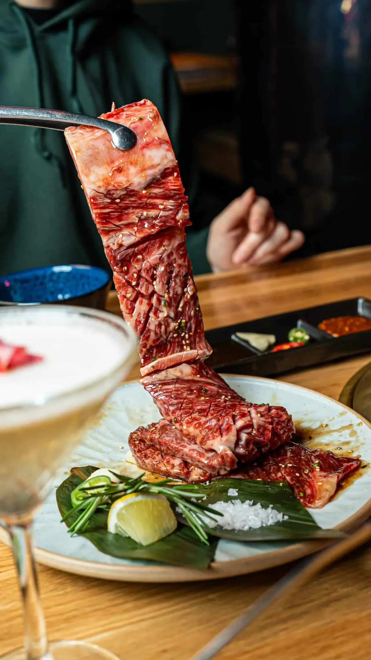 Sliced marbled beef short rib skewered and held up over a plate with lemon, rosemary, and sea salt, GYOJASANG Korean BBQ & Bar