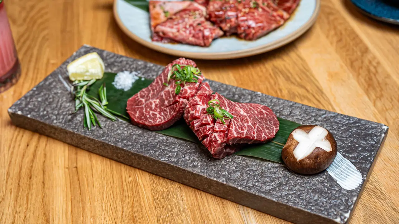 Sliced marbled raw beef cuts and a shiitake mushroom plated on a stone tray with lemon, rosemary, and salt, GYOJASANG Korean BBQ & Bar