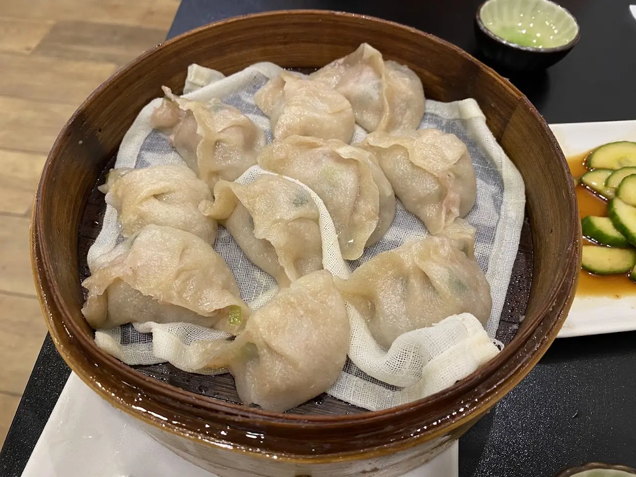Steamed gyoza in a paper-lined bamboo basket, with a small bowl of sauce beside it