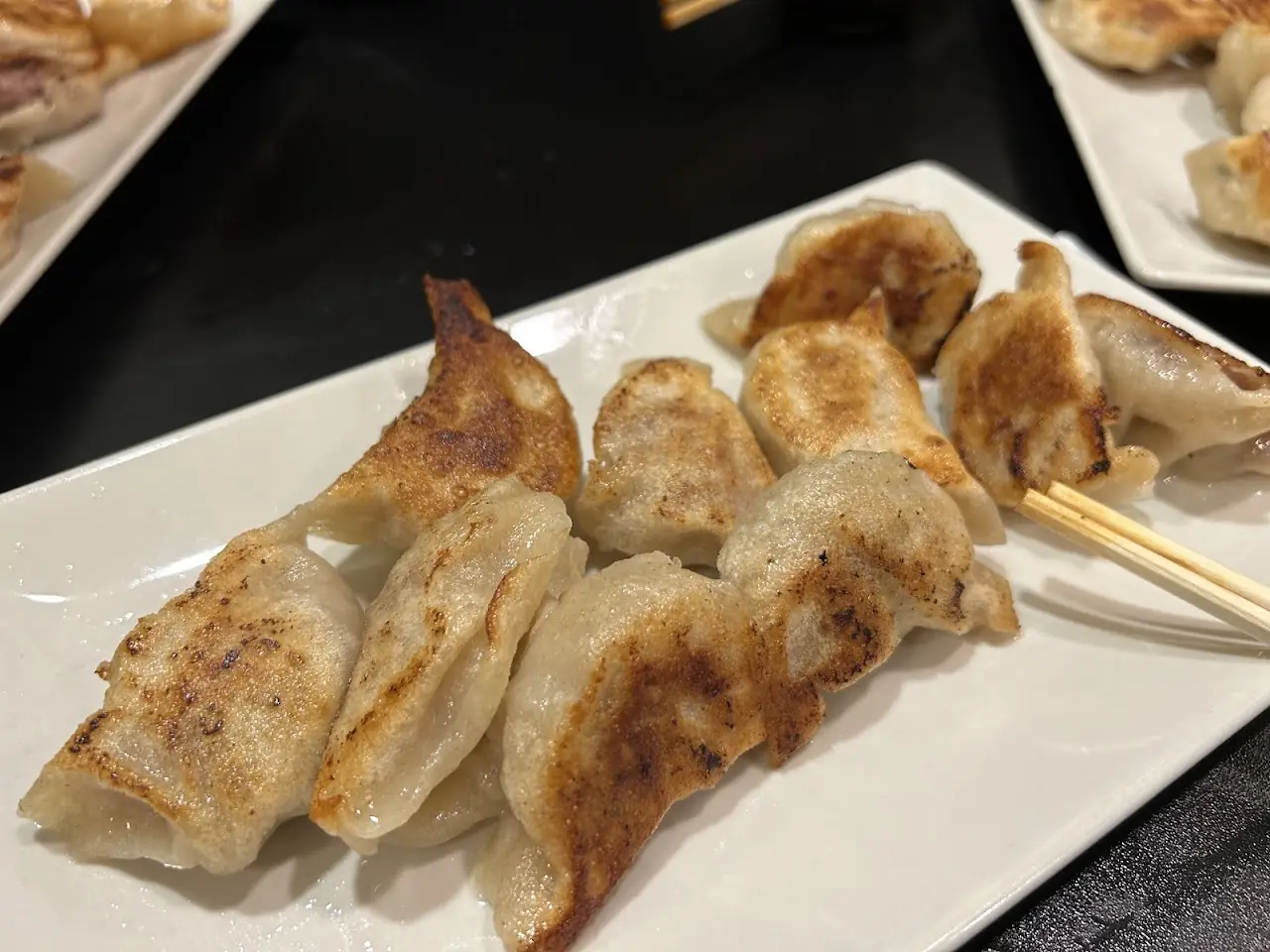 A plate of pan-fried gyoza with crisp golden bottoms and chopsticks