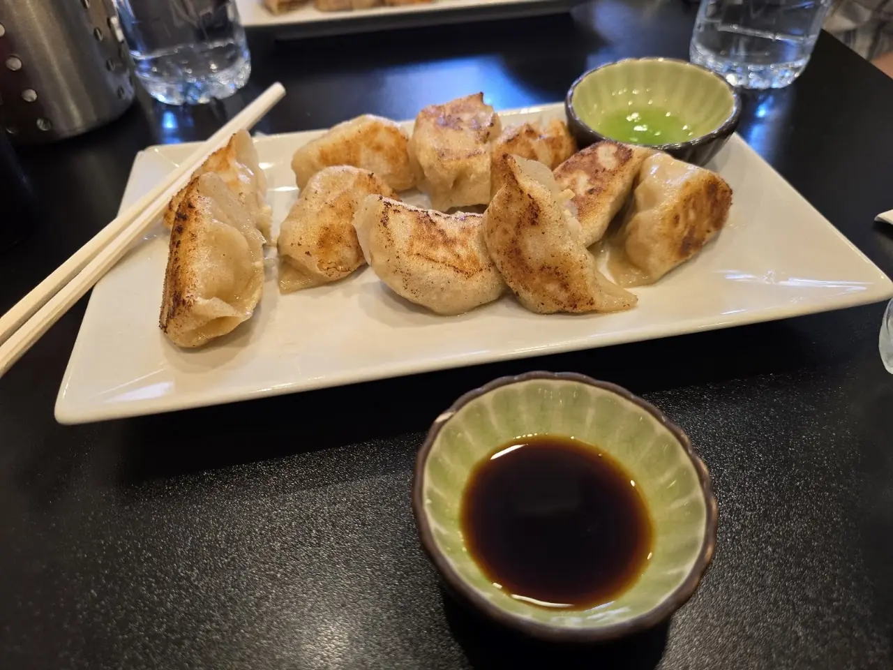 Pan-fried gyoza on a white plate with a bowl of soy dipping sauce