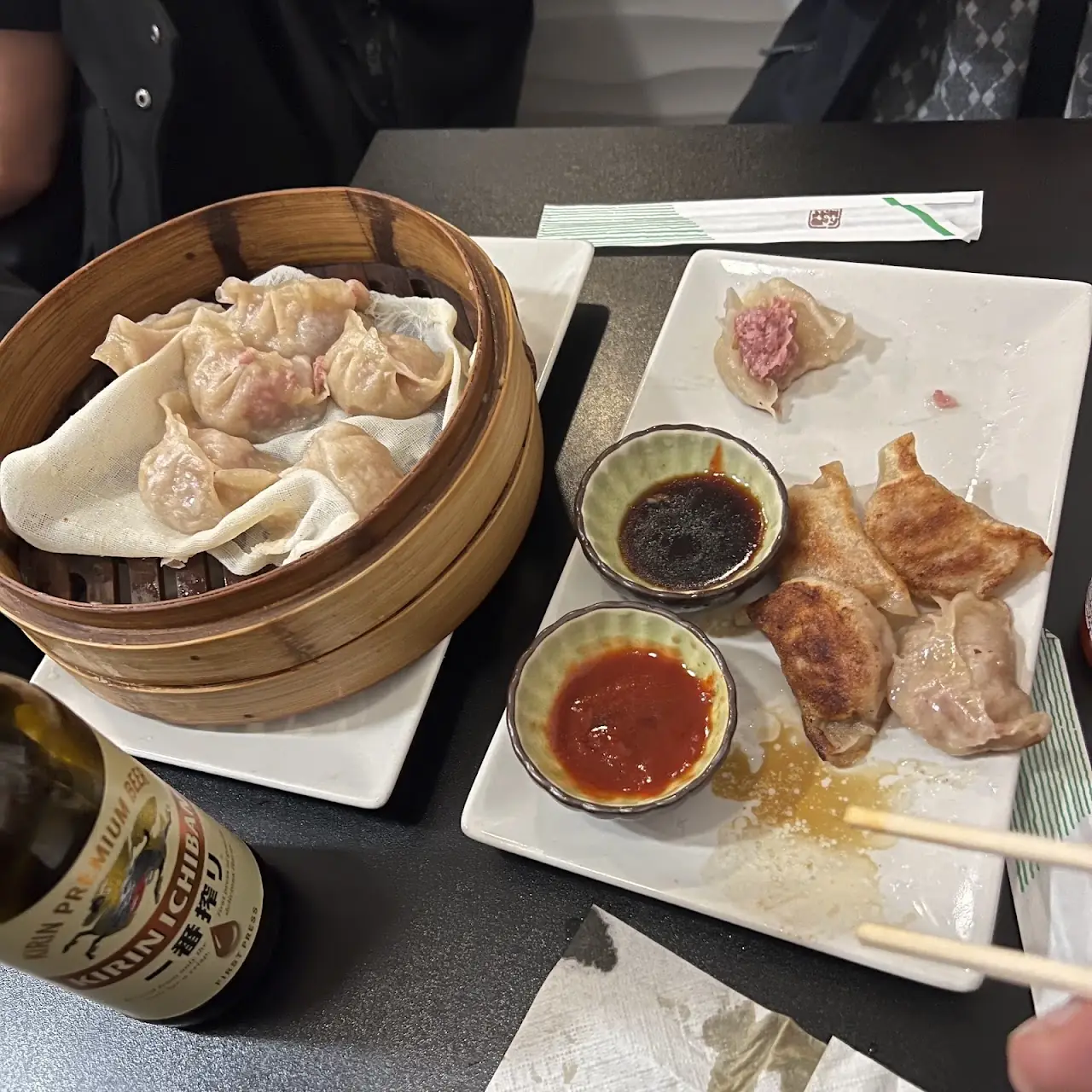 A bamboo steamer of dumplings next to a plate of fried gyoza with soy and chilli sauces