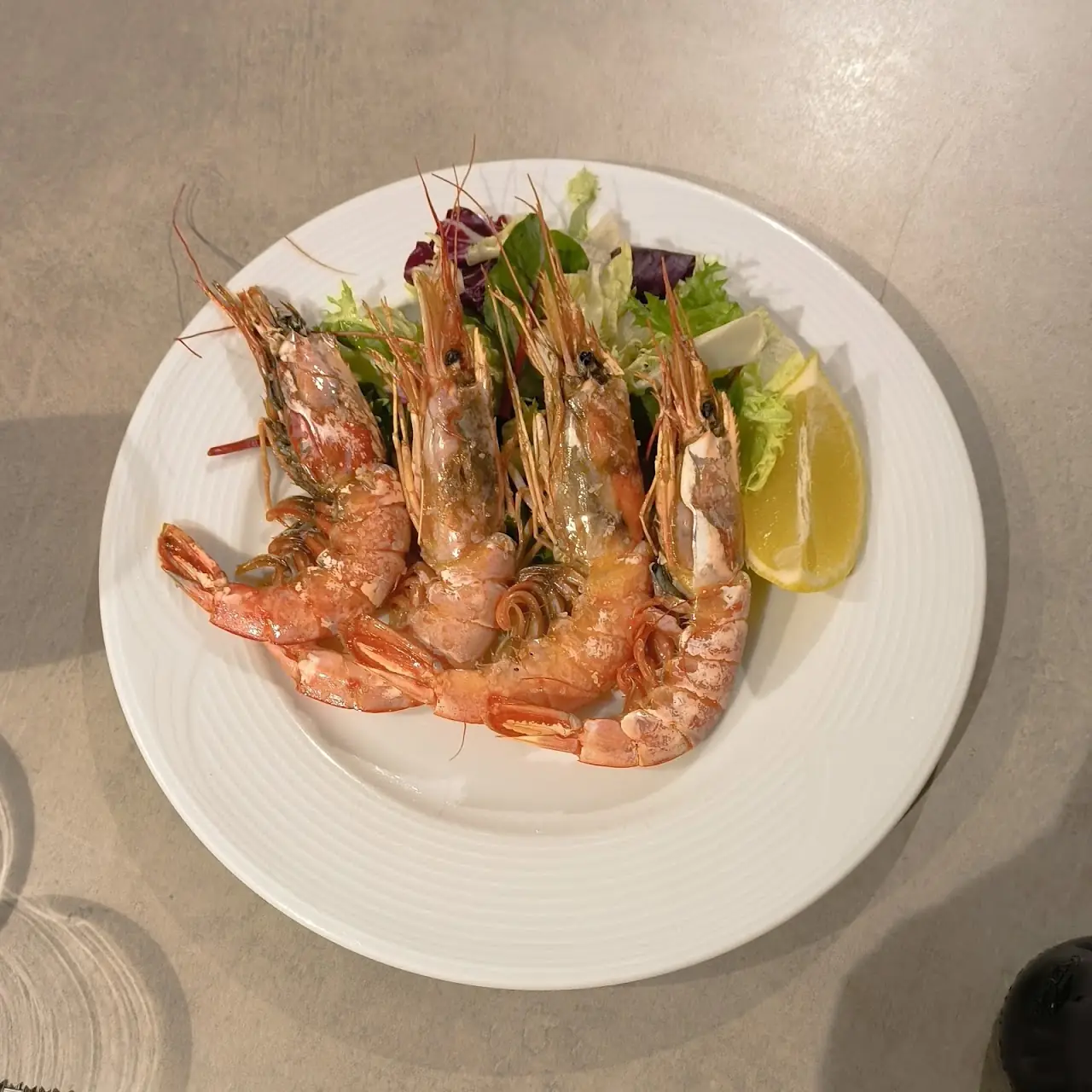 Grilled prawns with a lemon wedge and salad leaves on a white plate.