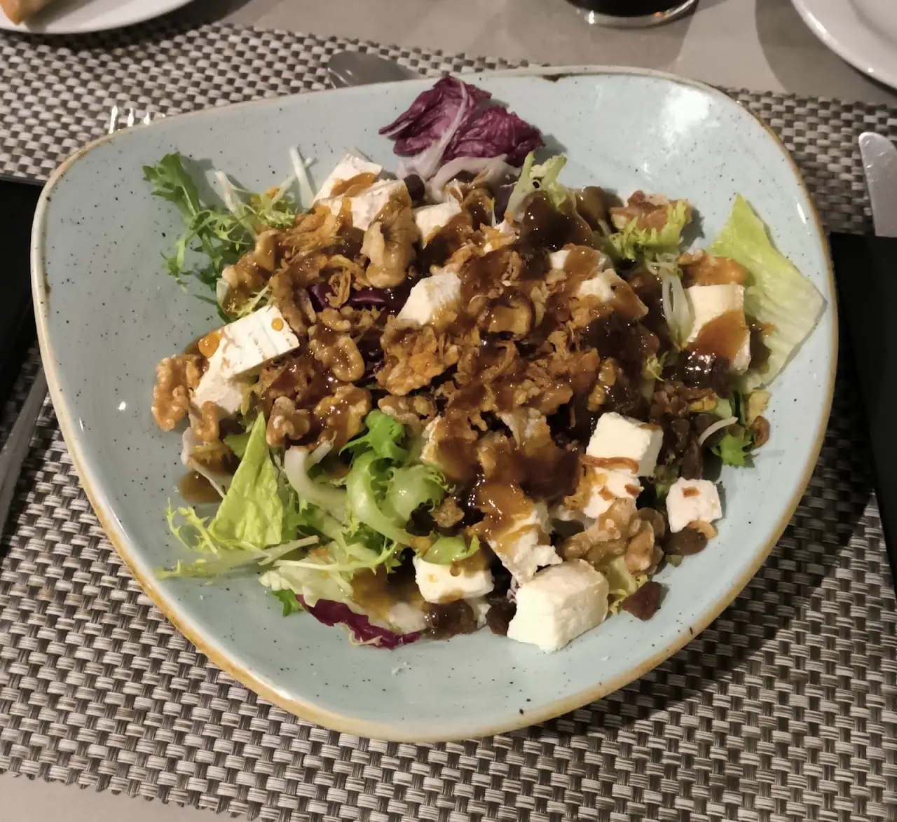 Salad with cheese cubes, walnuts and a dark dressing on a grey plate.