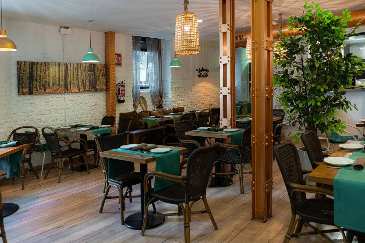 Dining room with wooden tables, green runners, rattan chairs, a Hakuna Matata wall sign and a large indoor tree