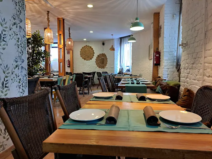 Restaurant interior with wooden tables set with teal runners and white plates, woven pendant lamps and botanical wall decor
