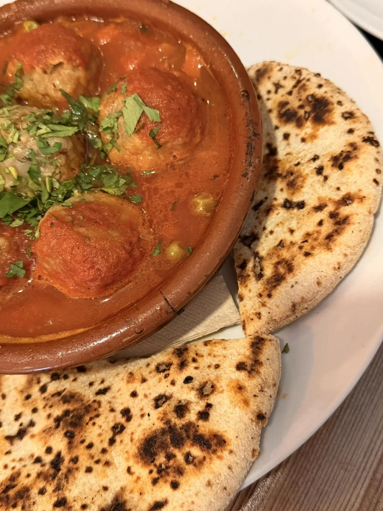 A tomato-based stew served in a clay bowl alongside grilled flatbread.