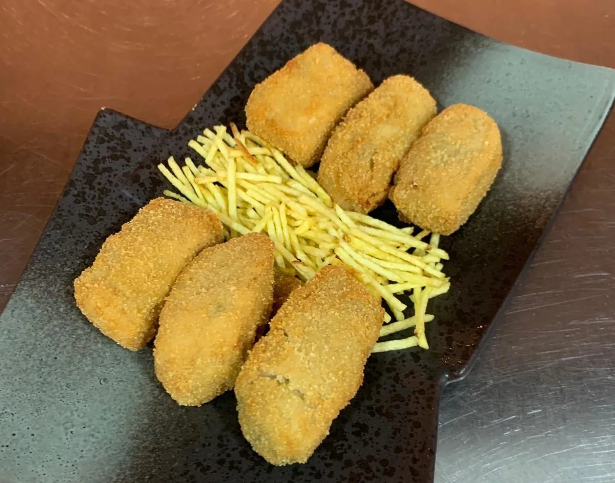 Five golden fried croquettes with a nest of fine fried potato strips on a dark plate