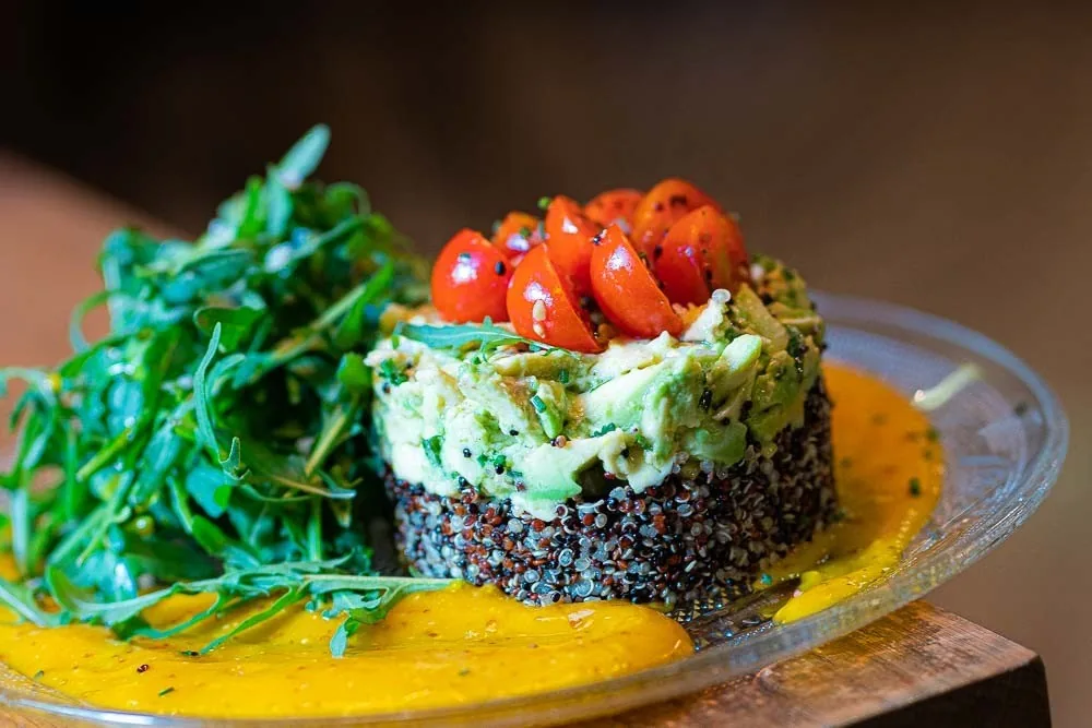A stack of quinoa and avocado topped with cherry tomatoes and rocket on a yellow sauce