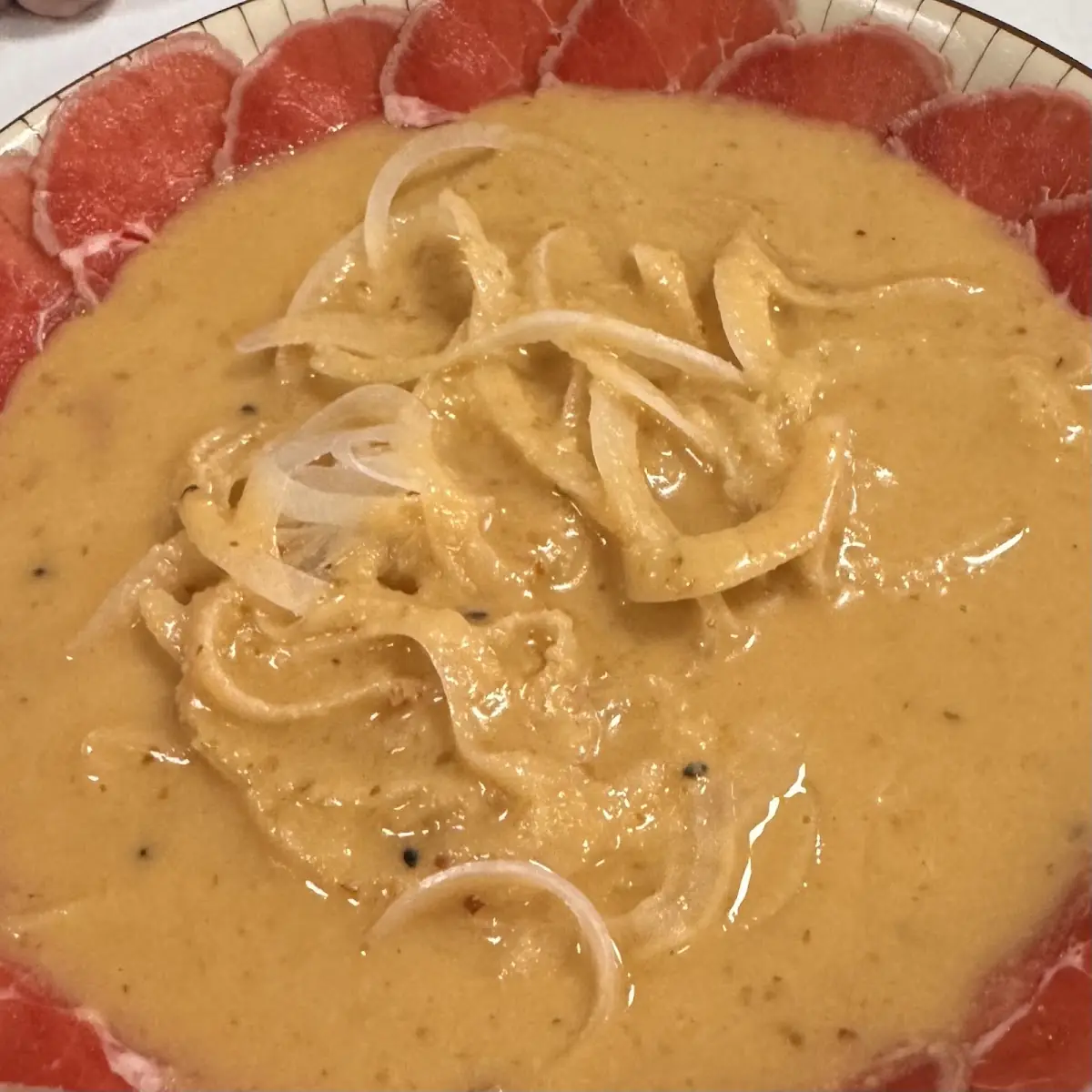 A carpaccio-style dish with sauce and onion at Hanaita