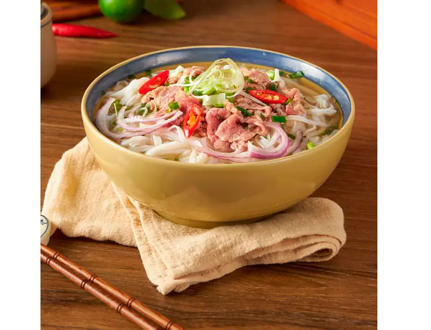 Bowl of Vietnamese pho with rice noodles, sliced beef, red chili, scallions, and pickled red onion in broth, served with fresh lime and chopsticks at Hanoi
