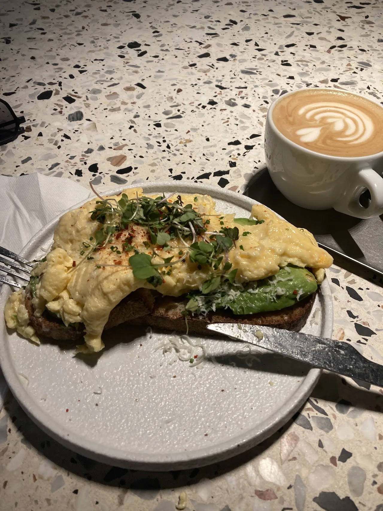 Avocado toast with herbs on a plate beside a latte