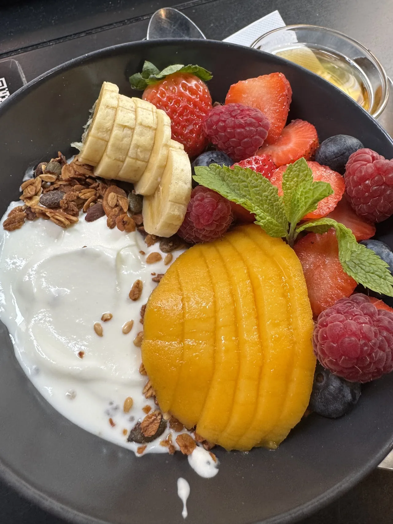 A bowl of granola with yogurt, banana, peach, and berries