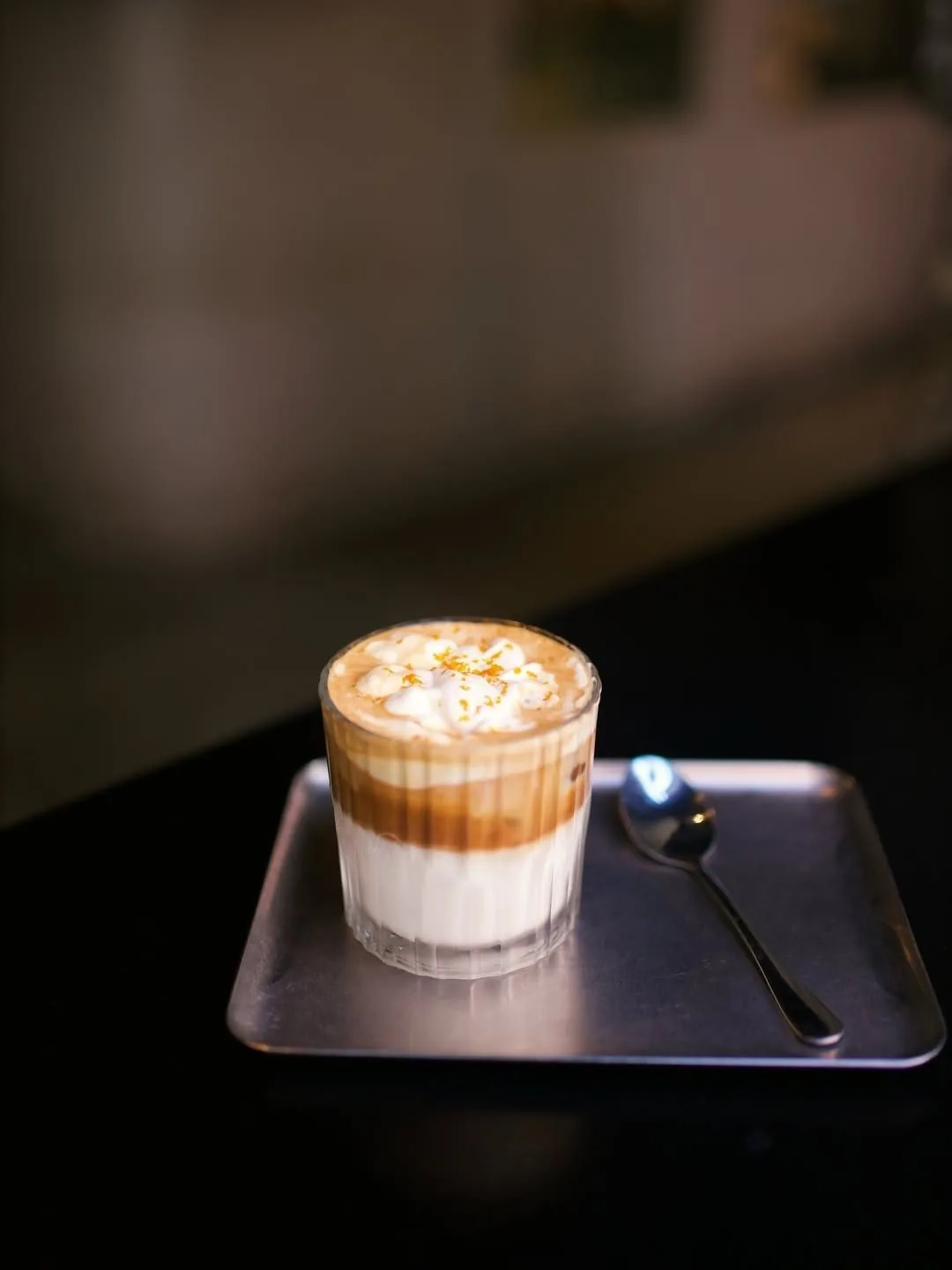 A layered coffee drink with foam in a glass on a small dark tray