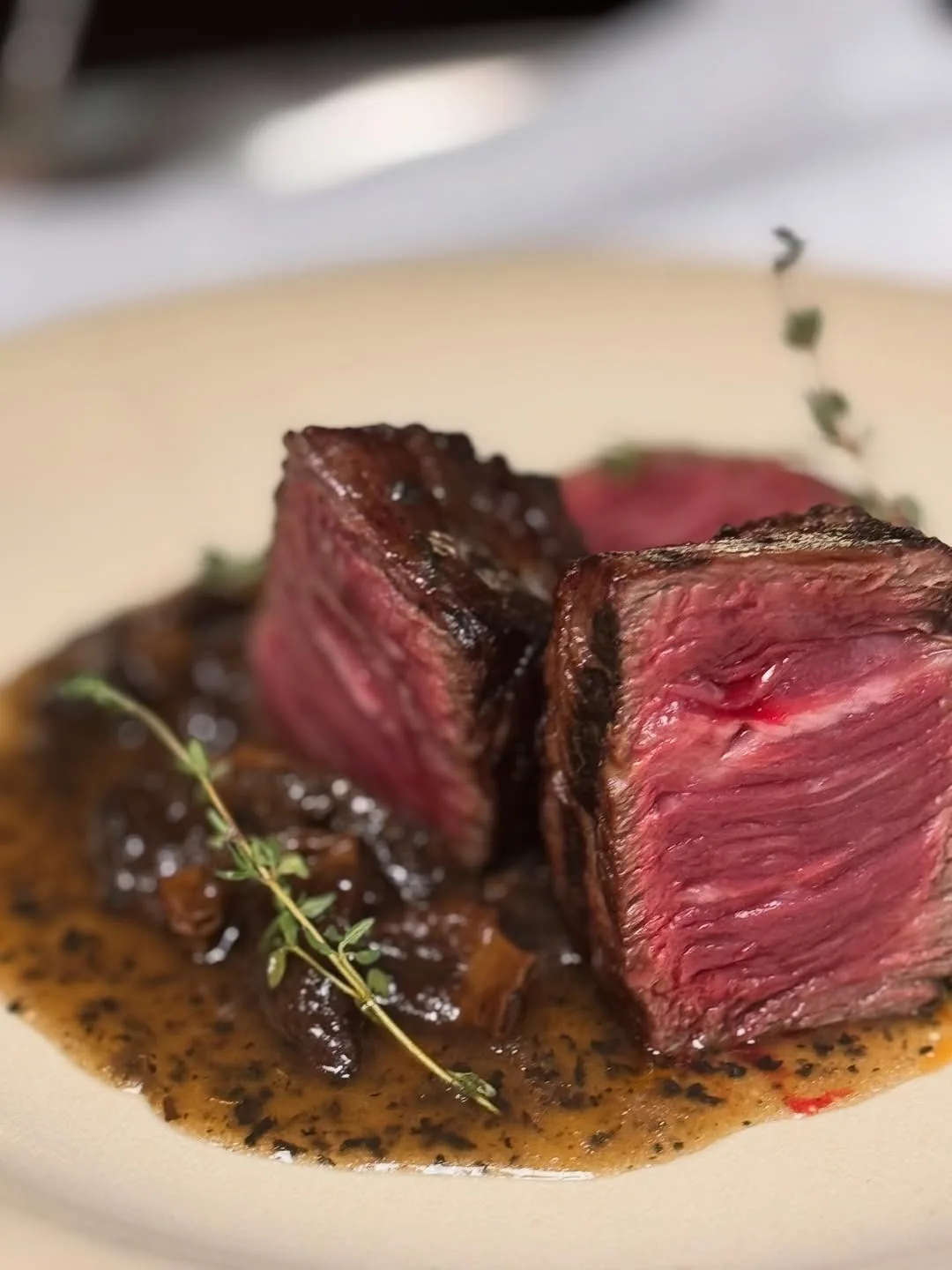A thick cut of medium-rare beef in dark sauce on a plate