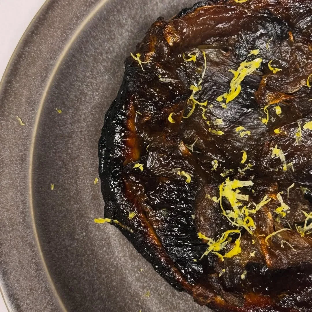 A dark browned tart with lemon zest on a grey plate