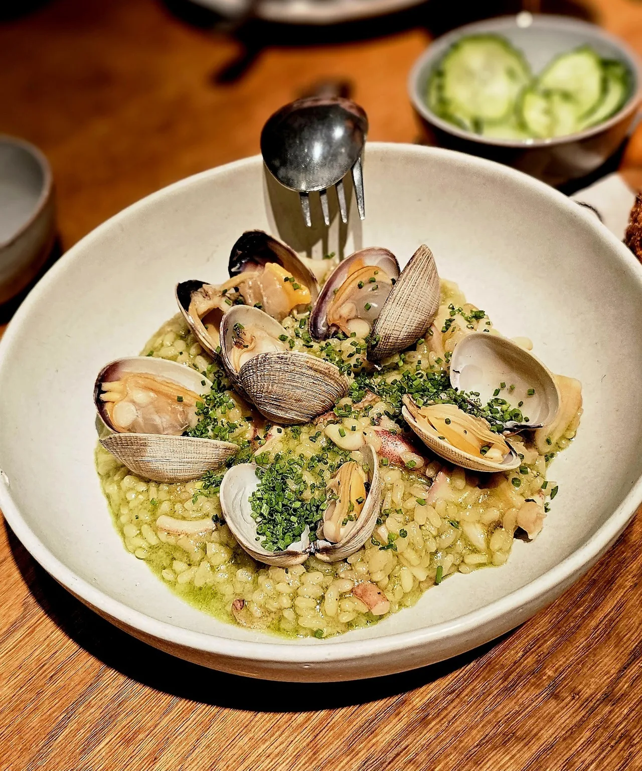 A bowl of green rice with clams and a metal jug