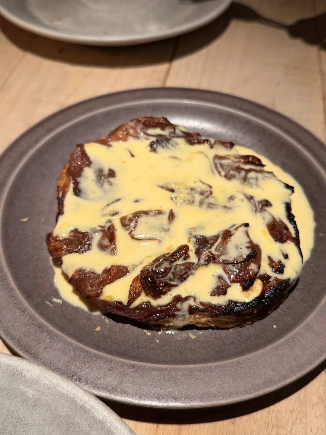 A dark plate holding a browned tart topped with a yellow sauce
